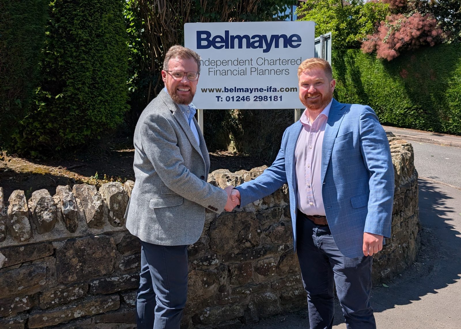 Belmayne managing partner Martin Birch, left, shaking hands with trainee financial planner Greg McMillan in front of the Belmayne sign