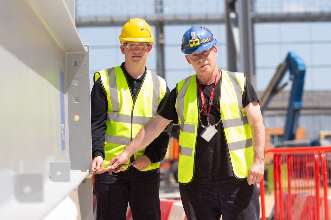 First year apprentice Joe Garrett and longest serving machinist Paul Haxton tighten the golden bolt on the last steel beam of the new machine shop